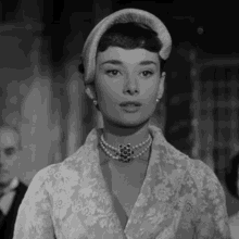 a black and white photo of a woman wearing a hat and pearls .