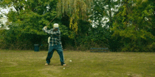 a man in a plaid shirt is jumping in the air in a park