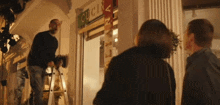 a man on a ladder stands in front of a store called cucina