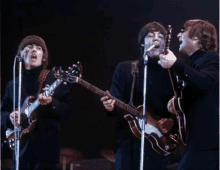 three men are singing and playing guitars on a stage