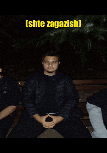 a man in a black jacket sits on a bench under a sign that says ' shte zagazish '