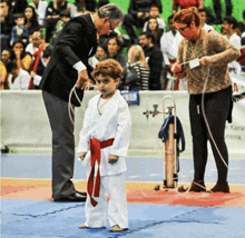 a little boy with a red belt is standing on a mat