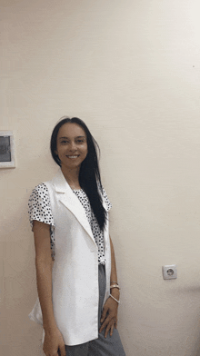 a woman wearing a white vest and a polka dot shirt is standing in front of a wall