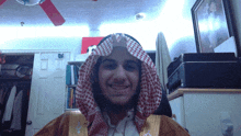 a man wearing a keffiyeh is smiling in a room