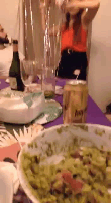 a woman is sitting at a table with a bowl of guacamole and a bottle of beer .