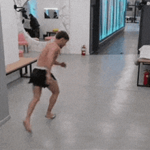 a shirtless man is dancing in a hallway with a fire extinguisher on the floor