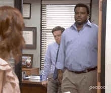 a man in a blue shirt and tie is standing in front of a woman in an office .