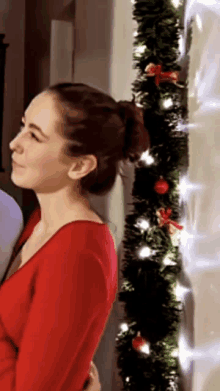 a woman in a red shirt is standing in front of a christmas tree