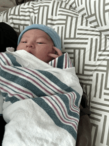 a baby wrapped in a striped blanket with a blue hat on