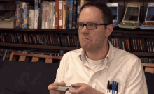 a man wearing glasses is playing a video game in front of a shelf full of video games including one called sonic