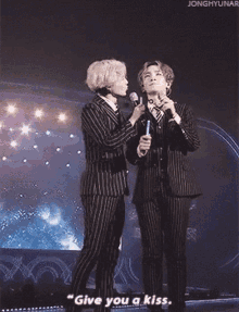 two men in suits are standing next to each other on a stage and one of them is holding a microphone .