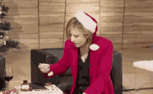 a woman wearing a santa hat and a red jacket is sitting at a table with a christmas tree in the background .