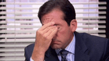a man in a suit and tie is rubbing his forehead with his hand .