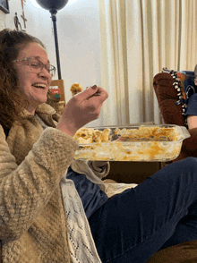 a woman sitting on a couch eating a casserole