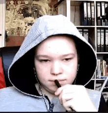 a person wearing a hoodie is holding a pen in his mouth