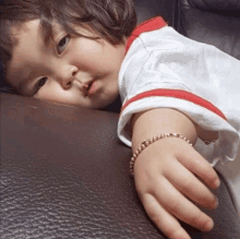 a little girl wearing a bracelet is laying on a brown leather couch