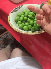 a person is holding a cucumber over a bowl of green olives .