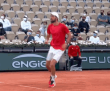 a man in a red shirt and white shorts is running on a tennis court in front of an engie sign