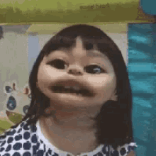 a little girl in a polka dot dress is making a funny face with her mouth open .