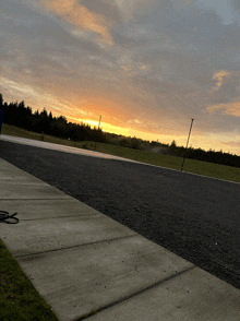 a sunset over a road with a concrete sidewalk