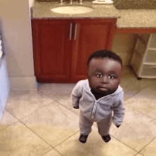 a small baby is standing on a tiled floor in a bathroom .