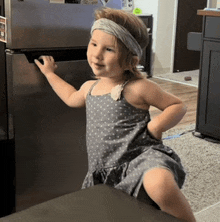 a little girl wearing a headband is standing in front of a stainless steel refrigerator