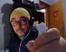 a man wearing headphones and a yellow beanie holds a small object