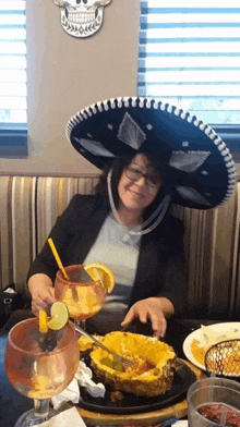 a woman wearing a sombrero sits at a table with a plate of food and drinks