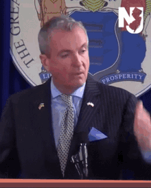 a man in a suit and tie stands in front of a podium with the new jersey state seal behind him