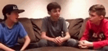 three boys are sitting on a couch and talking to each other .