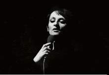 a woman sings into a microphone in a black and white photo