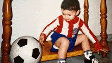 a young boy in a red and white striped shirt sits next to a soccer ball with the number 9 on his socks