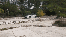 a silver car is parked on the side of a road near a stone wall