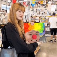 a woman is holding a picture of a clown with a red nose and a rainbow wig