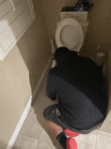 a man kneeling down in front of a toilet with a bag of tissues on the floor