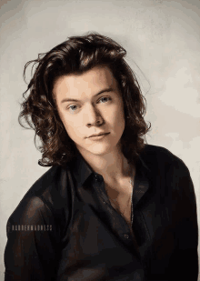 a young man with long curly hair is wearing a black shirt and a necklace