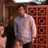 a man in a striped shirt stands in front of a red block wall