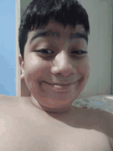 a young boy without a shirt is smiling for the camera while taking a selfie .