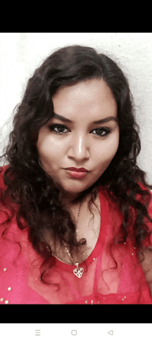 a woman with curly hair is wearing a red top and a necklace with a heart shaped pendant