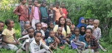 a group of children are sitting in the grass with a woman in the middle .