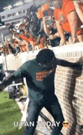 a man in a green shirt is dancing in front of a brick wall .
