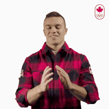 a man in a plaid shirt is clapping his hands in front of a maple leaf and the olympics logo