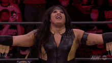 a female wrestler is standing in a ring with her arms outstretched .