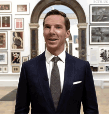 a man in a suit and tie stands in front of a wall of pictures with the letters bcth-uk on the bottom right