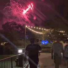 a man wearing a black shirt that says ' fireworks ' on it walks in front of a firework display