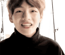 a close up of a young boy wearing a black turtleneck sweater and smiling .