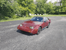 a red car is parked in a parking lot with trees in the background and the temperature is 100 degrees