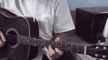 a man in a white shirt is playing a black acoustic guitar