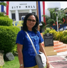 a woman in a blue shirt stands in front of a building that says city hall