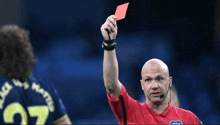 a referee holds up a red card in front of a player wearing a jersey with the number 27 on it